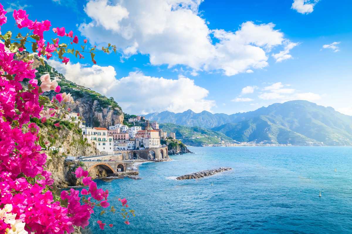 Famiglia con bambini piccoli che gioca sulla spiaggia sabbiosa di Amalfi, fondale basso, colori vivaci, atmosfera rilassata, sfondo di case color pastello e mare calmo